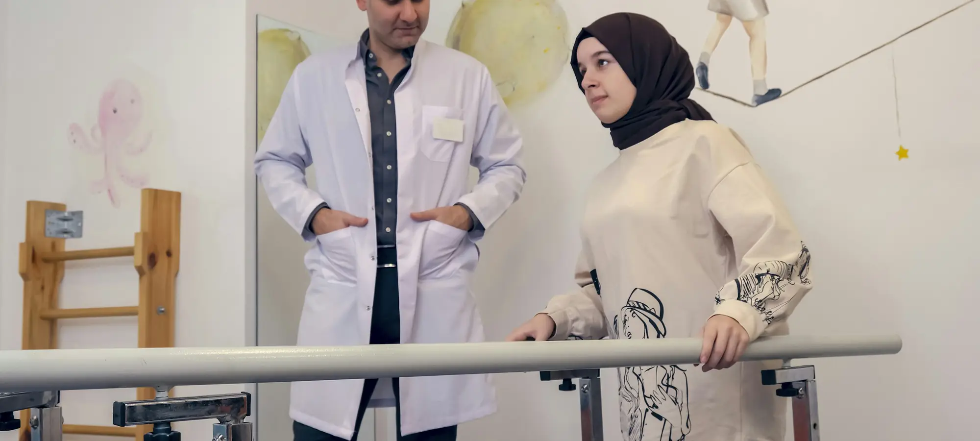 Hekim, paralel bar yanında hastayla konuşuyor