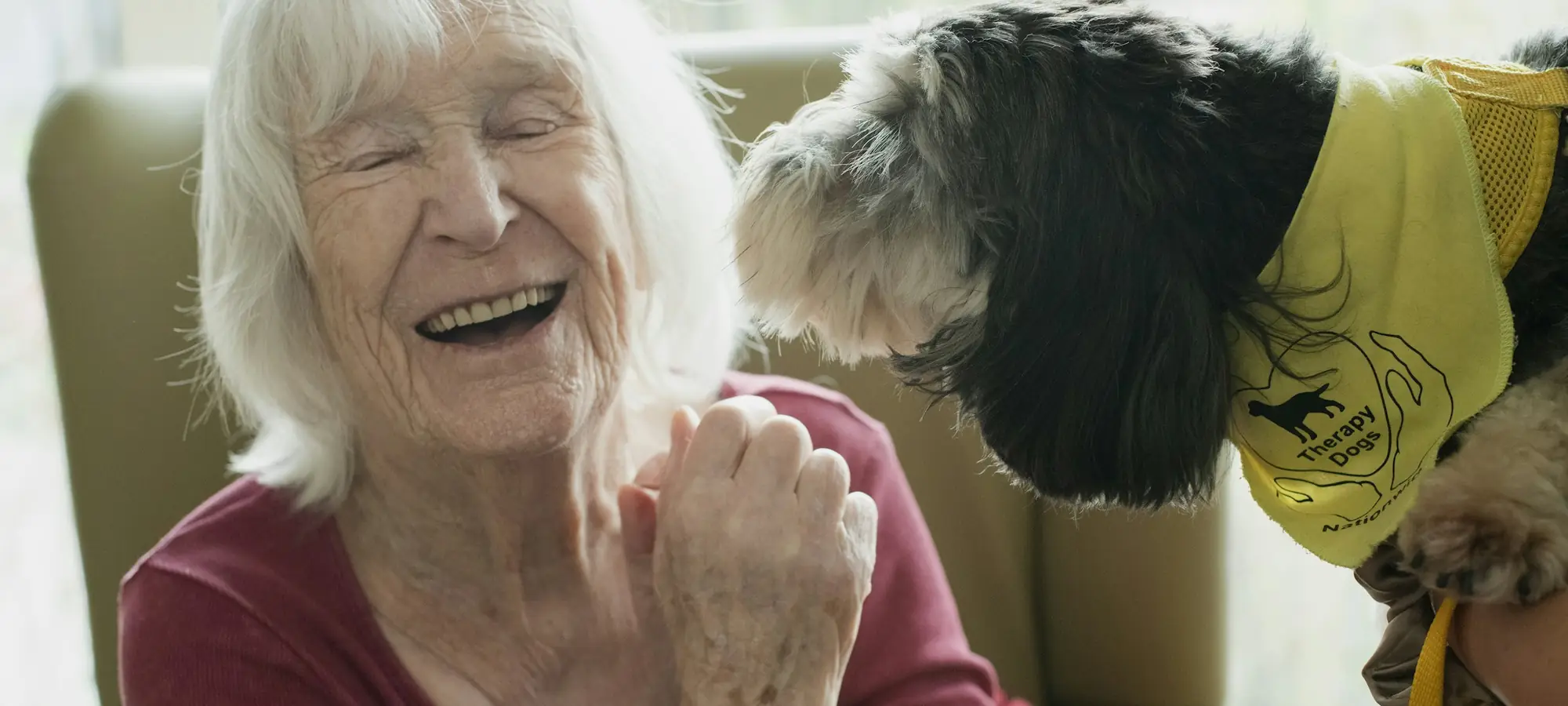 Yaşlı bir kadın evinde köpeğiyle gülüyor